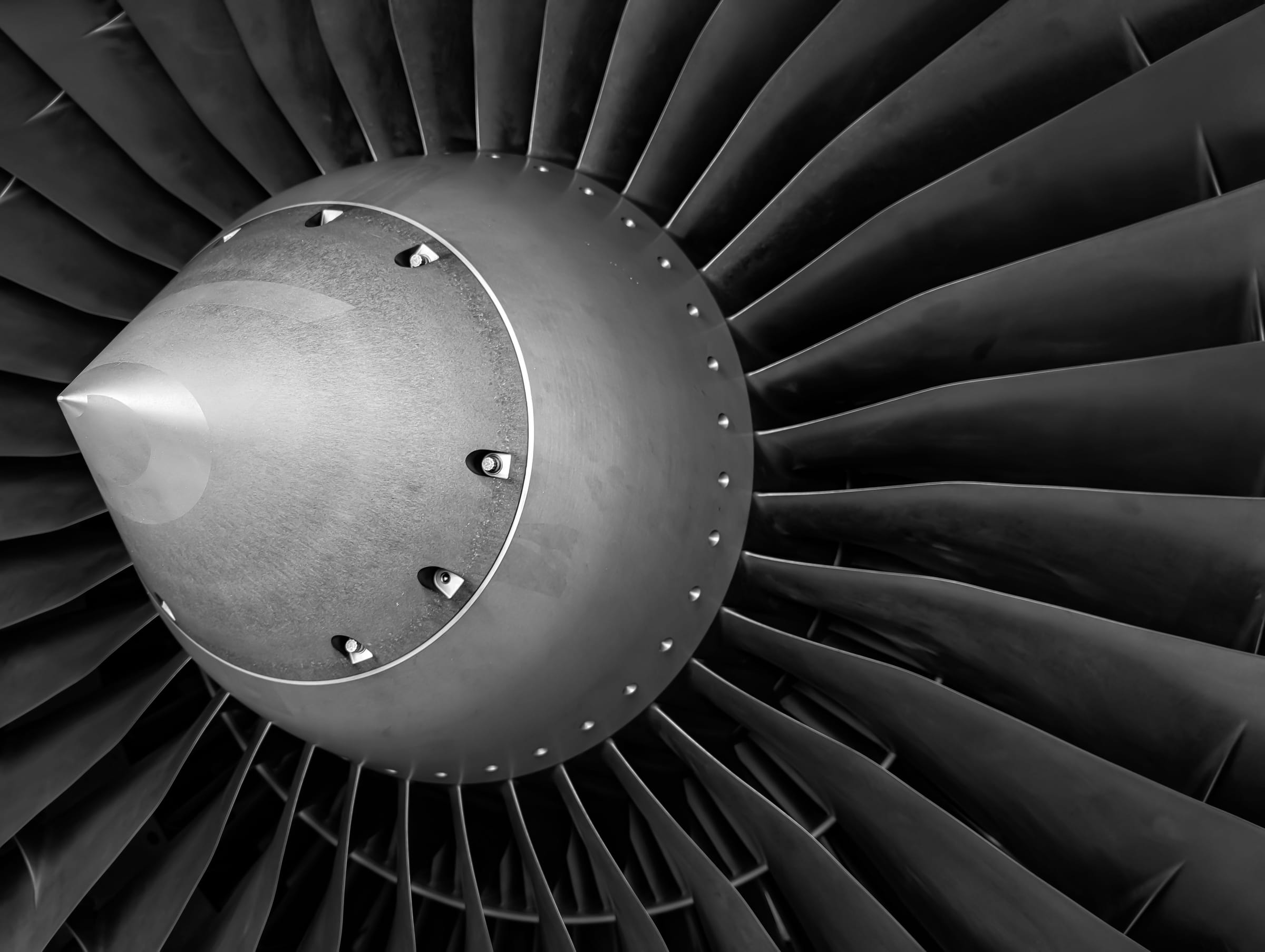 Close-up of the front of a jet engine, with the polished nose cone lit from one side and the fan blades curving away into shadow.