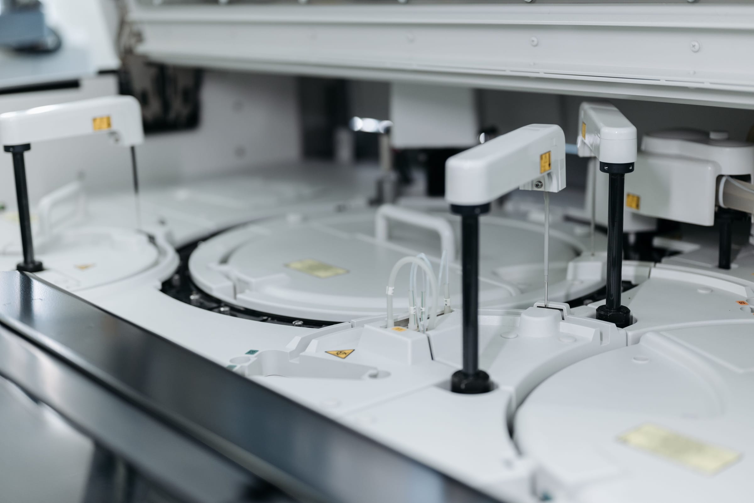 Interior of an automated clinical analyser with white sample carousels and vertical pipetting arms.